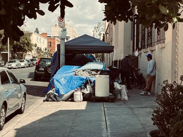 A sidewalk tent shelter with two men nearby on a city street.