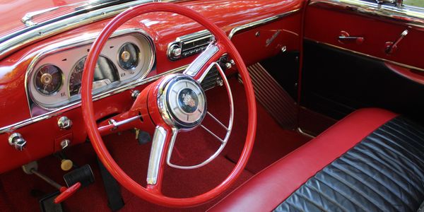 Interior of a vintage car with red and black leather seating and a classic steering wheel.