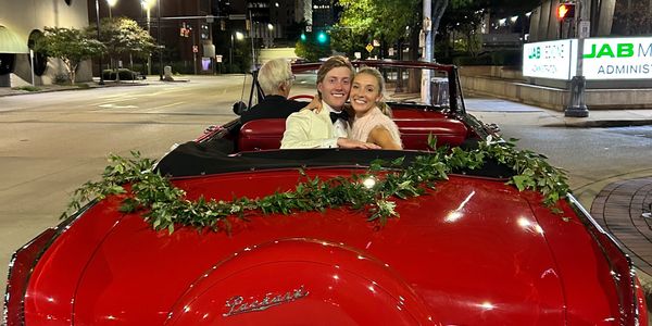 Couple smiling in a red classic Packard convertible at night.