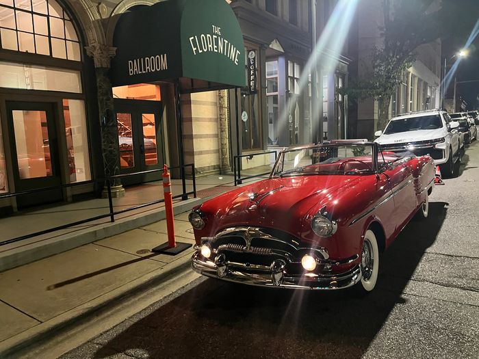 A classic red convertible car parked outside The Florentine Ballroom at night.