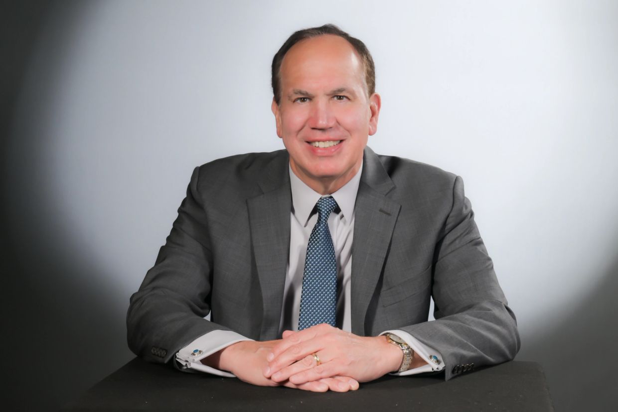 A smiling man in a gray suit and blue tie sitting at a table.
