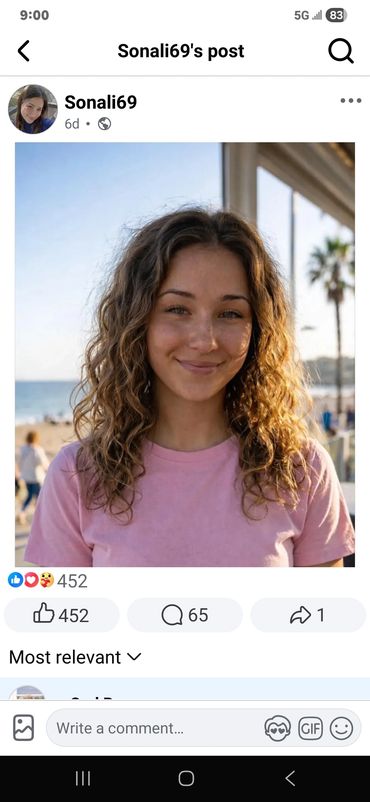 Young woman with curly hair smiling at the beach in a pink shirt.