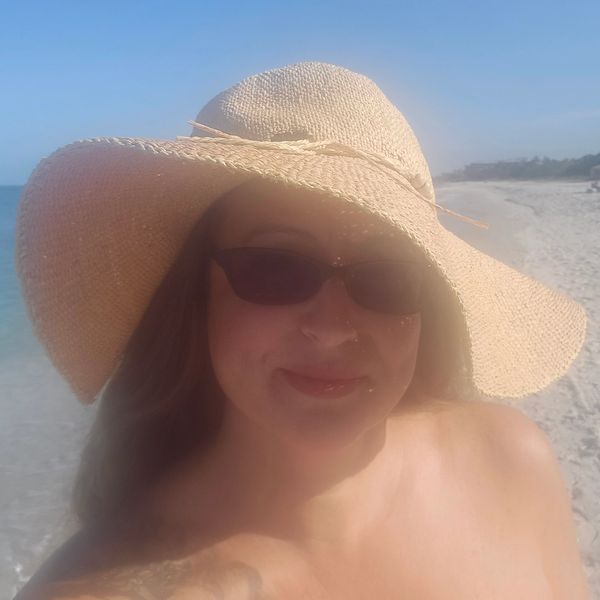 Woman in large sunhat and sunglasses on beach.