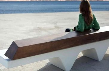 A woman in green sitting on a modern wooden bench by the water. bancas de acero inoxidable
papeleras
paradas