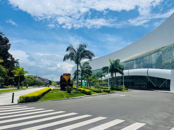 Modern building with palm trees and a train under a bright blue sky.