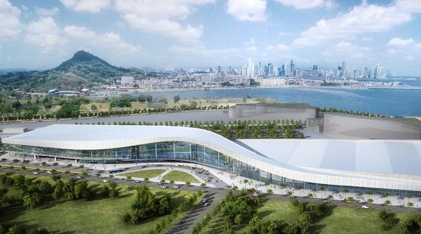 A large modern building with a curved roof near water and a city skyline.