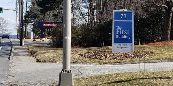 Sign for The First Building at 71 with leasing info on a roadside grassy area.