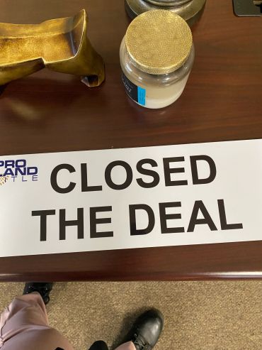 A "Closed the Deal" sign on a wooden desk with decorative items.