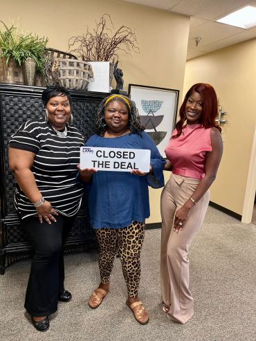 Three women smiling, holding a sign that says "Closed the Deal."