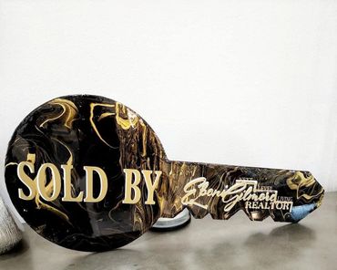 Decorative key-shaped sign with "SOLD BY" and realtor's name.