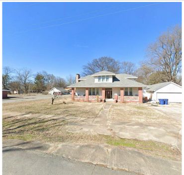 Single-story brick house with a large front yard under clear blue sky.