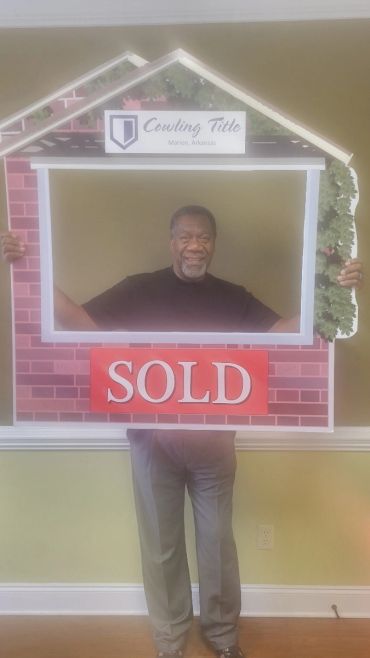 Man holding a house-shaped frame with a SOLD sign, smiling.