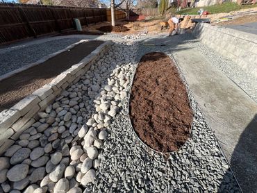 Man working on a landscaped backyard with rocks and mulch beds.