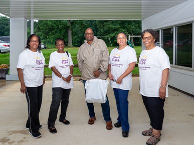 Five volunteers from Blessed to Help, wearing matching t-shirts, stand together holding a donation.
