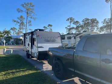 Truck towing a Pioneer Trail Blazer camper in a sunny campground.