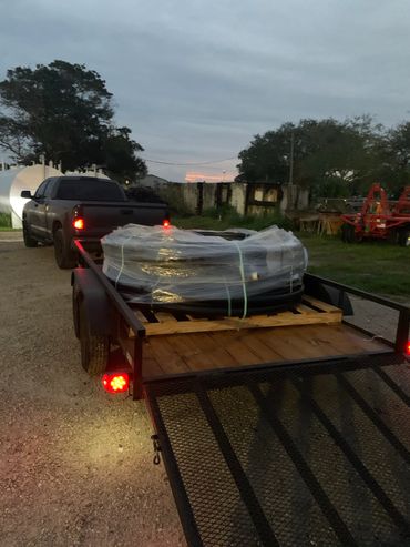 Pickup truck towing a trailer with wrapped materials on a pallet at dusk.