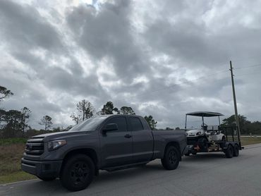 Gray pickup truck towing a trailer with a golf cart on a cloudy day.