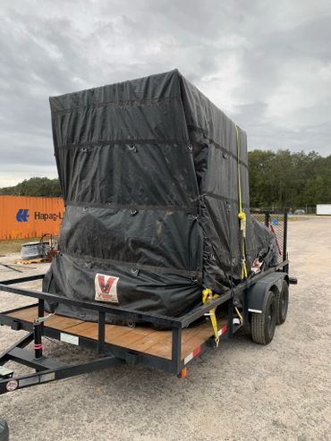 Large black tarp-covered load secured on a trailer with yellow straps.