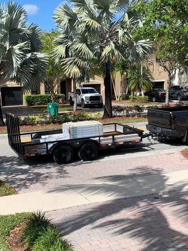 A pickup truck towing a trailer loaded with construction materials on a residential street.