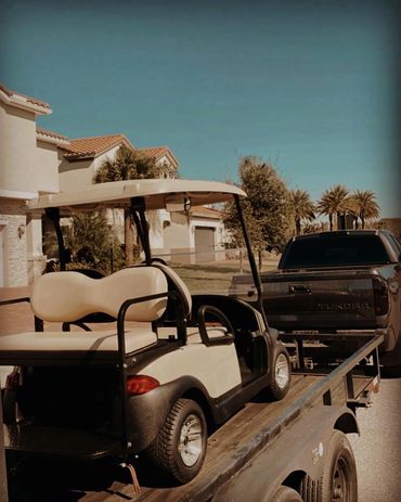 Golf cart loaded on a trailer behind a pickup truck in a suburban neighborhood.