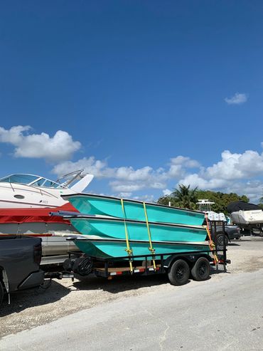 Three turquoise boats strapped on a trailer under a clear blue sky.