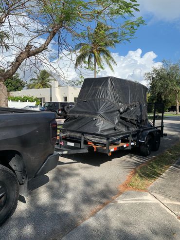 Black pickup truck towing a trailer covered with a black tarp on a sunny street.