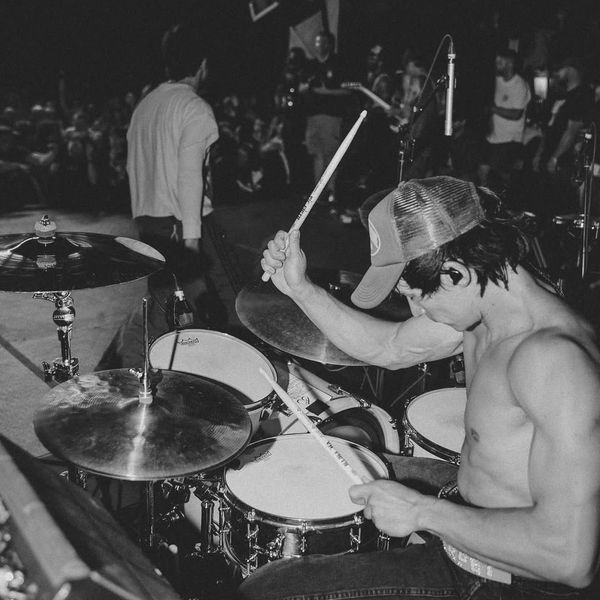 Shirtless drummer passionately playing at a live concert.