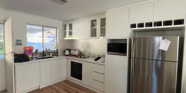 Modern white kitchen with stainless steel fridge and wooden floor.