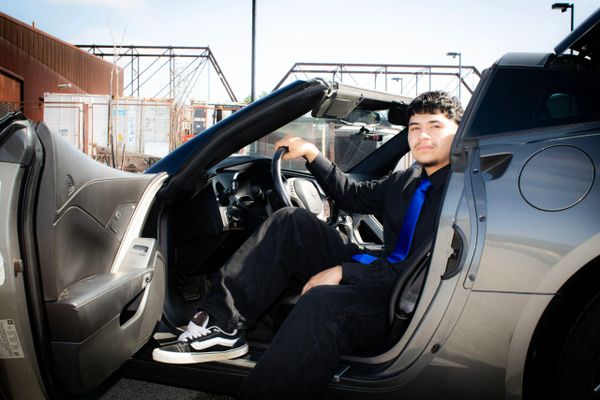 Young man sitting in a sports car with the door open, smiling.