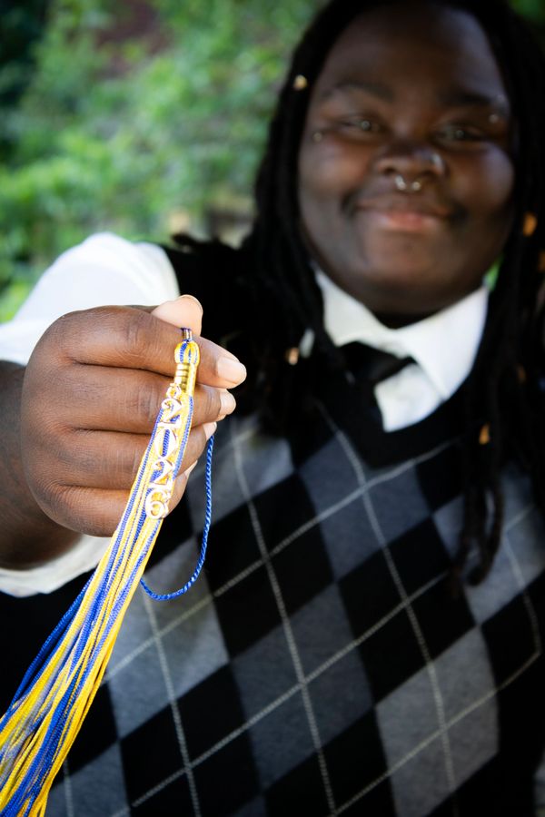 Person smiling and holding a blue and yellow graduation tassel with the year 2026.