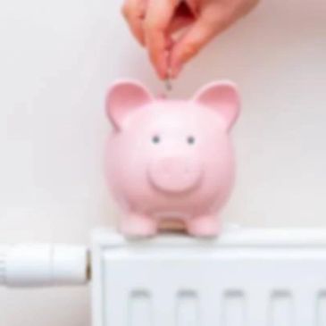 Hand putting coin into pink piggy bank on radiator.