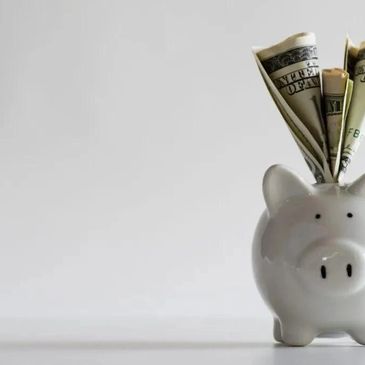 White piggy bank with rolled dollar bills sticking out on a plain background.