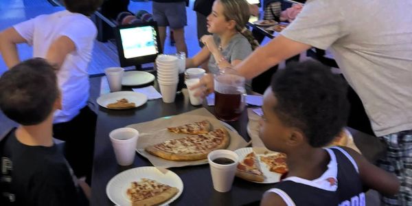 Kids enjoying pizza and drinks at a bowling alley table.