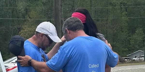 Three people in a group hug outdoors, showing support and unity.