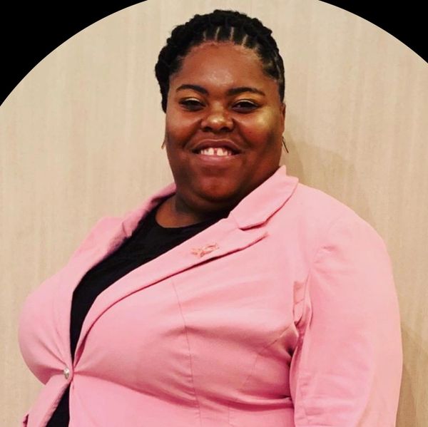 Smiling woman wearing a pink blazer and black top.