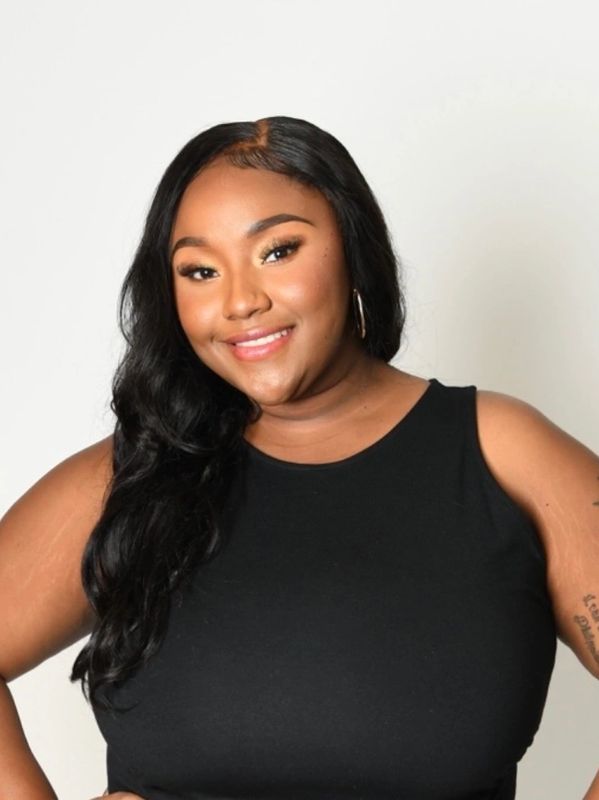 Confident woman smiling in a black sleeveless top against a plain backdrop.