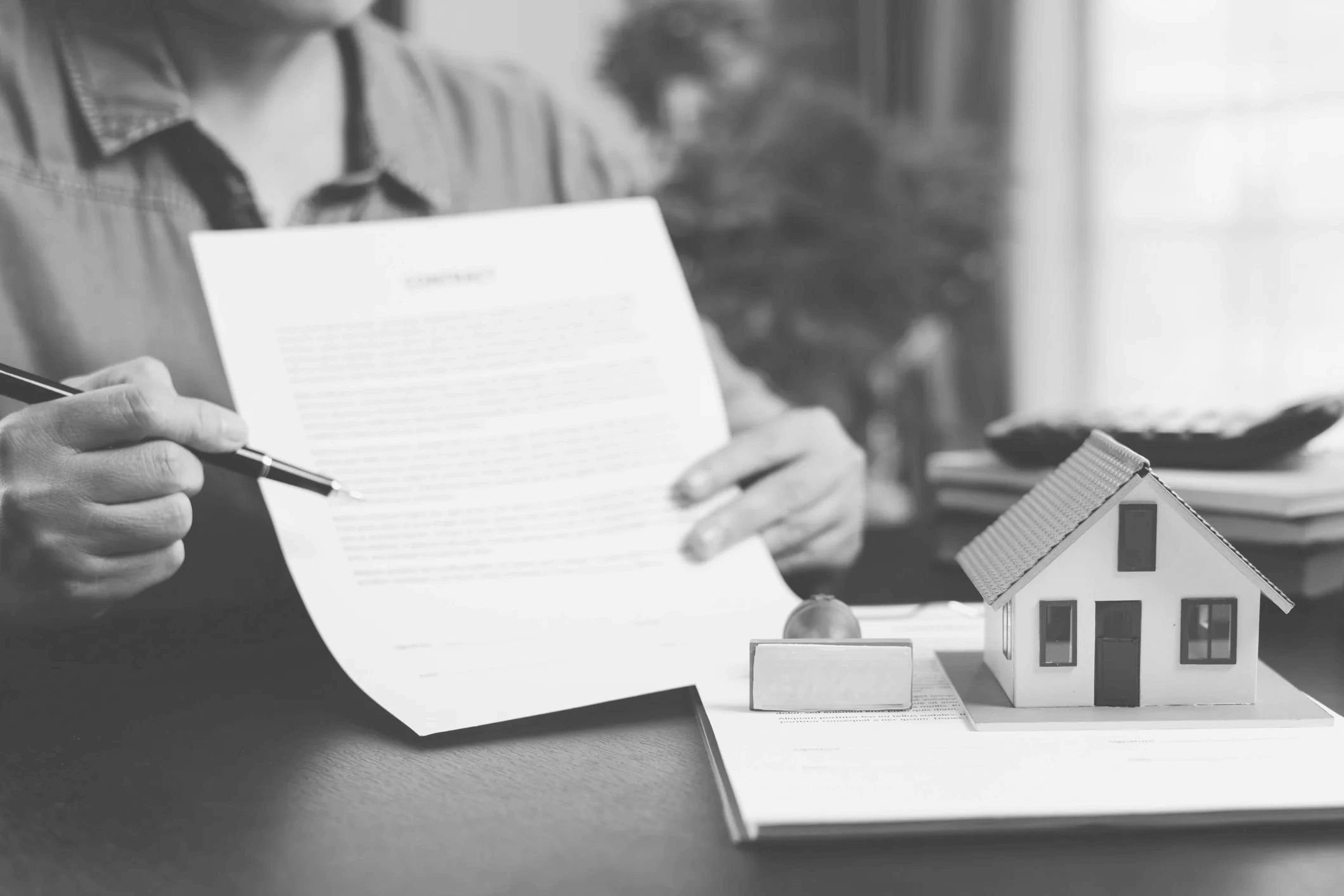 Person reviewing a contract with a model house and stamp on the table.