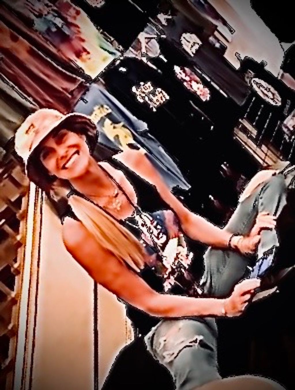 Smiling woman wearing a bucket hat and ripped jeans sitting indoors.