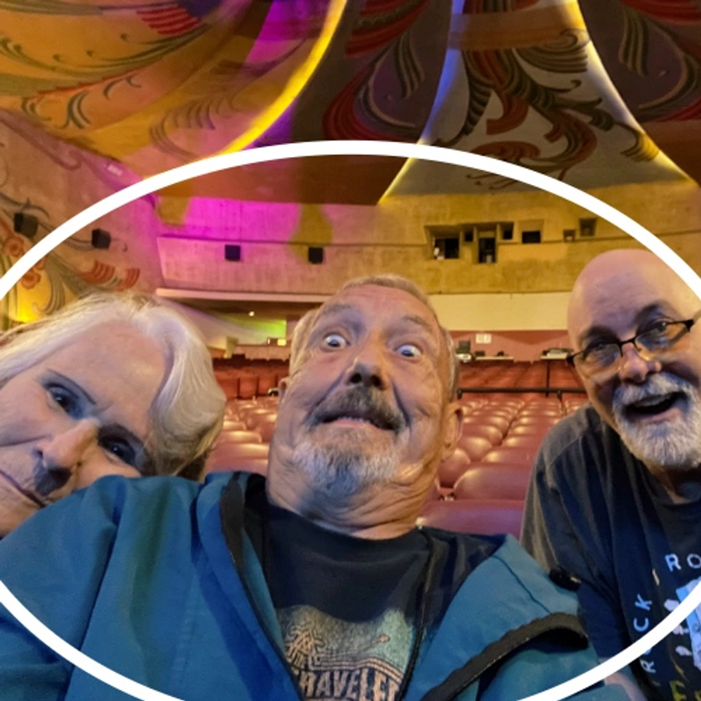 Three men making funny faces in an empty theater with colorful decorations.