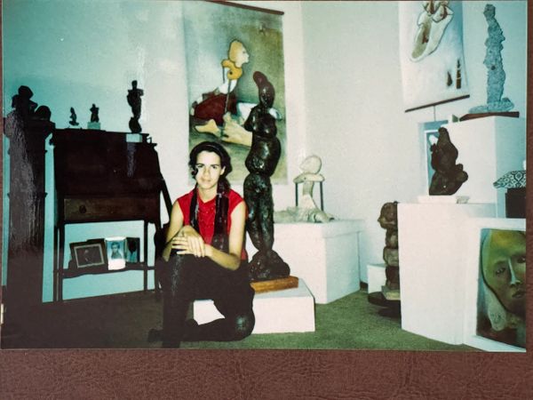 A woman sitting on the floor in an art gallery surrounded by sculptures and paintings.