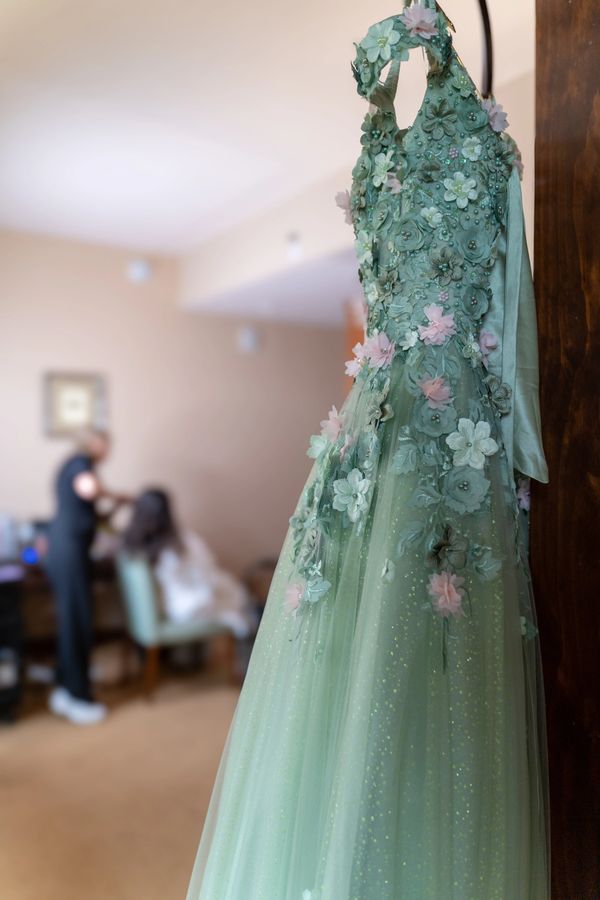Elegant green dress adorned with delicate floral appliques hanging in a room.