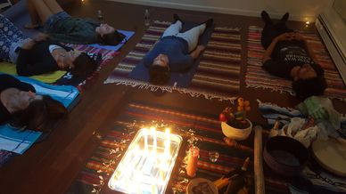 People lying on mats surrounded by candles and ritual items.