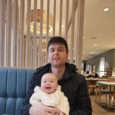 A man holding a smiling baby in a cozy restaurant booth.