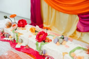 Long white table cake with brightly colored florals and fruit. Photo: The Wickerts Photography