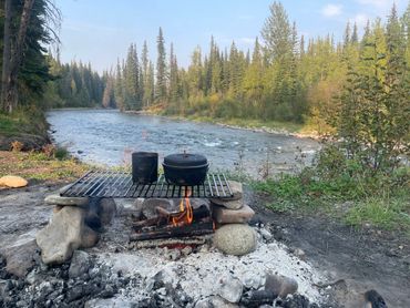 Camping fire with cooking pots by a river in a forest.