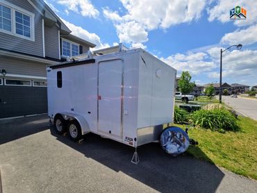 Pine Box camper exterior with awning, door, window, solar panels & spare tire in daylight