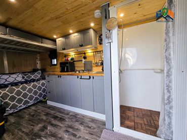 Pine Box interior featuring shower, kitchenette, smoke detector, lights & convertible sleeping area