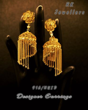 Elegant gold designer earrings with hanging chains displayed on a black hand model.