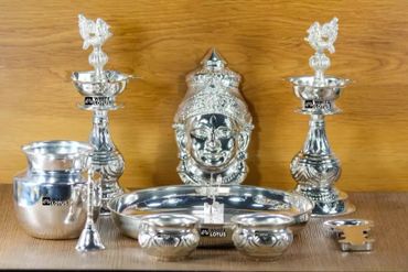 Silver pooja set with deity idol and traditional lamps on wooden surface.