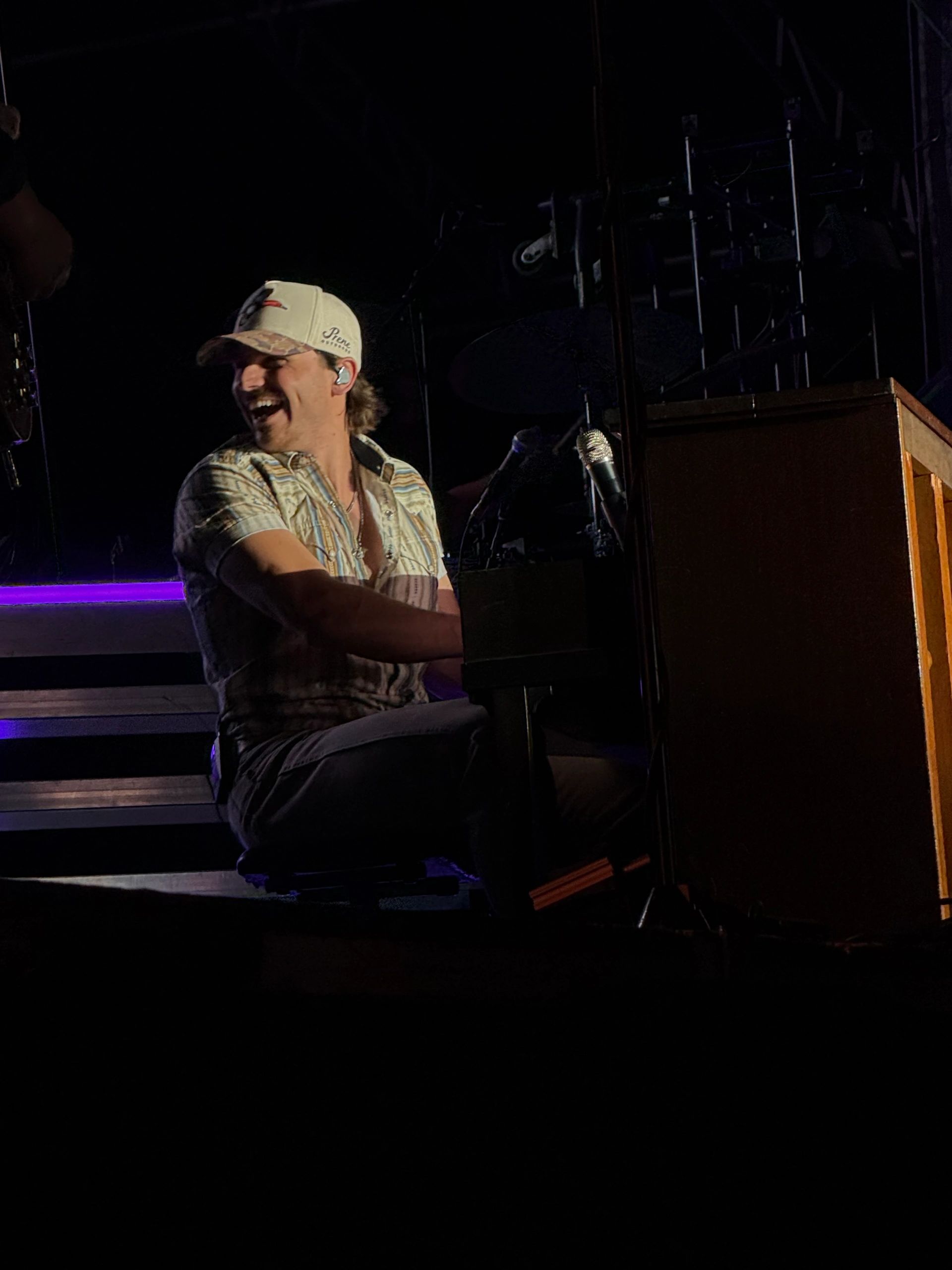 Man joyfully playing piano on stage with purple lighting.